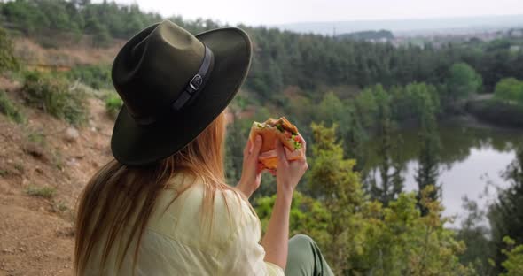 Young traveling woman eating sandwich while taking a break enjoying scenic view.