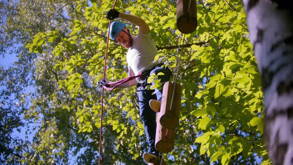 A Man Carefully Walks on Logs Suspended in the Air Between Trees in the Forest