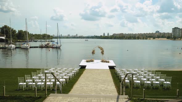 Weeding Arch Decorated with Pastel Faded Flowers and White Chairs Lake on the Background Slow Motion