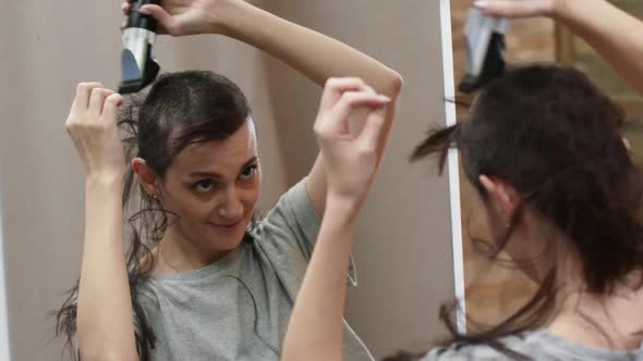 Woman Brunette Hairdresser Shaves Hair with a Machine for Haircut Standing Near the Mirror and