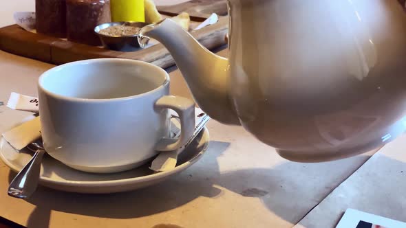 Closeup on a Table in a Restaurant Poured Green Tea From a White Teapot Into a White Cup