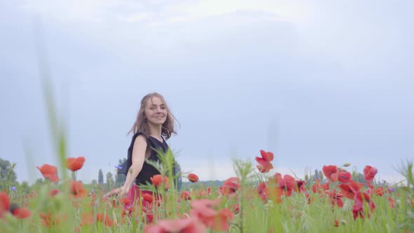 Cute Young Woman Running and Dancing in a Poppy Field Smiling Happily. Connection with Nature