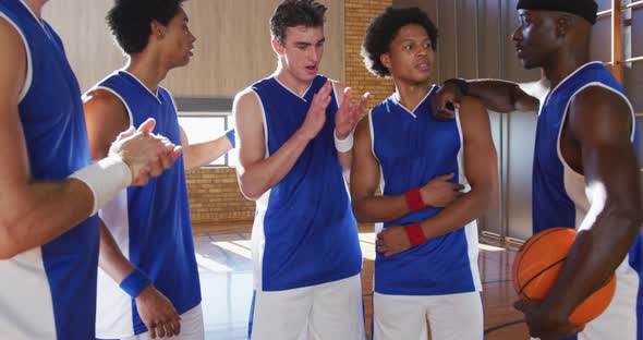 Diverse male basketball team and coach in huddle discussing game tactics