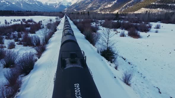 Train in a valley followed in winter snow oil tanks flyover