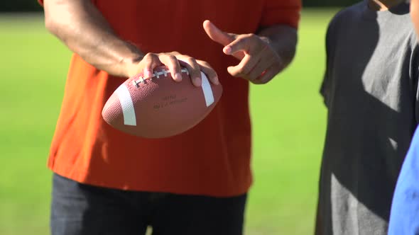 A father teaching his sons how to play American football.