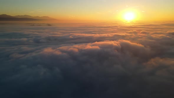 Aerial shot of flying over a layer of clouds at sunrise