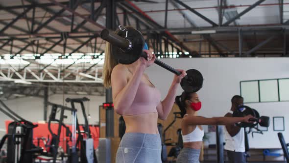 Fit caucasian woman wearing face mask exercising using barbell in the gym