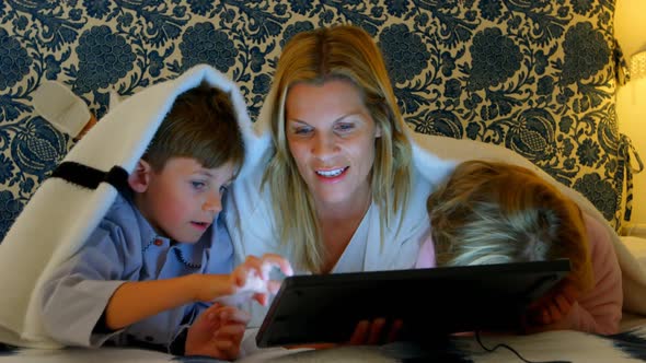 Front view of young Caucasian mother with her son and daughter using digital tablet on bed in bedroo