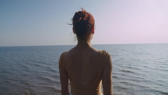 Back View of Redhead Slim Caucasian Woman Admiring Beauty of Sea Standing Outdoors at Dawn