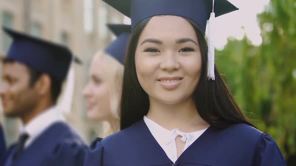 Asian girl in academic dress smiling posing at camera during graduation ceremony