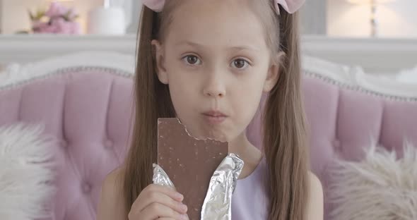 Close-up of Happy Little Girl Chewing Chocolate at Home, Satisfied Face of Pretty Brunette Caucasian