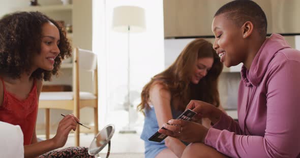 Diverse group of happy female friends trying makeup and talking at home