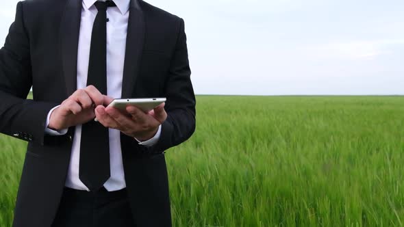 A Man Examines a Barley Crop with a Tablet in His Hands