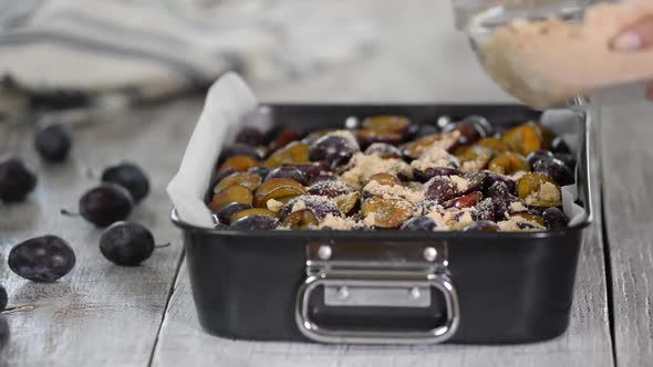 The process of making a fruit pie. Woman hands sprinkle crumble on the plum cake.