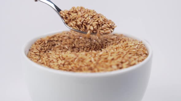 Flax seeds are mixed with a dessert spoon in a white cup.