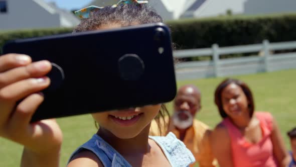 Front view of cute little black girl with family clicking selfie on mobile phone in the park 4k