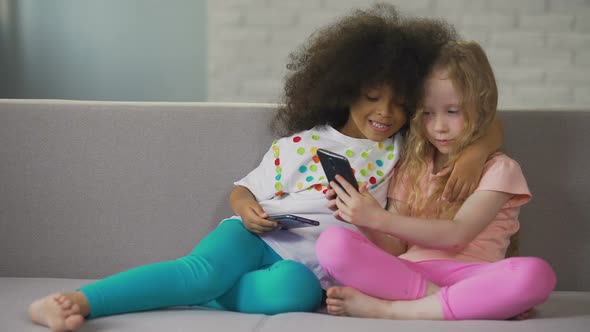 Multiracial Sisters Sitting on Couch, Hugging and Taking Selfie on Smartphone