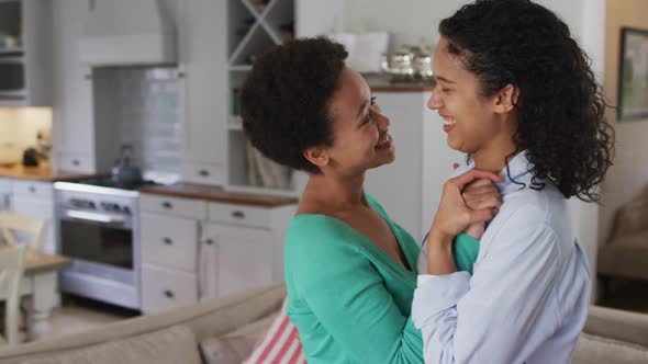 Romantic mixed race lesbian couple dancing in sitting room