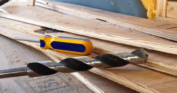 A drill bit and a screwdriver with plywood boards on the construction site of a new building.