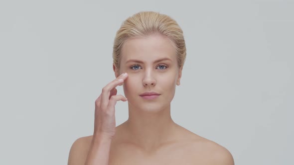 Studio portrait of young, beautiful and natural blond woman applying skin care cream. F