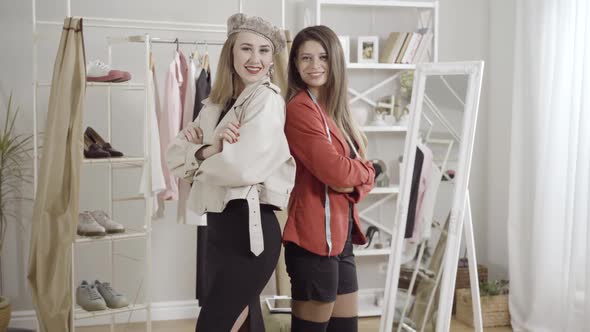 Two Confident Young Positive Women Standing Back To Back Posing in Atelier