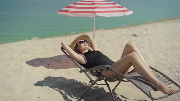 Wide Shot of Relaxed Beautiful Woman Lying on Sun Lounger and Smiling. Portrait of Happy Young Slim