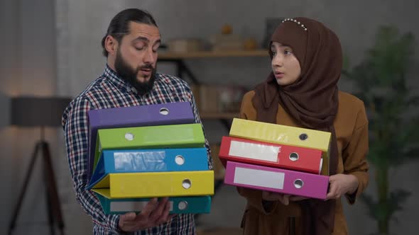 Tired Middle Eastern Couple Standing in Home Office Holding Document Folders Sighing