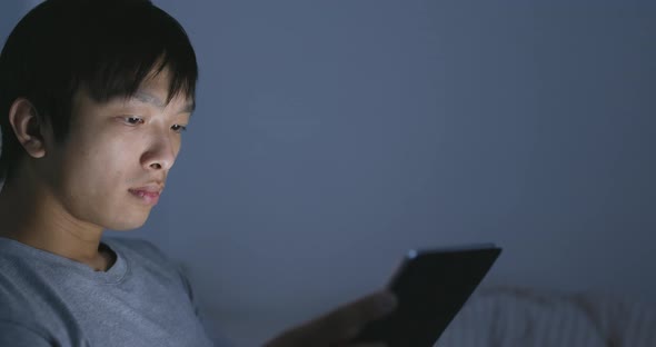 Man using tablet computer on bed at night 