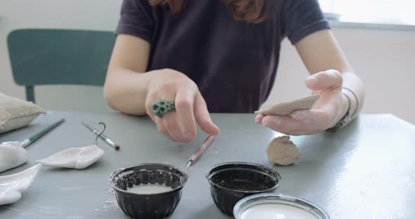 Woman Making Doll Ceramic Part. Female Sitting and Creating Ear for Doll at Home at Table. Pottery