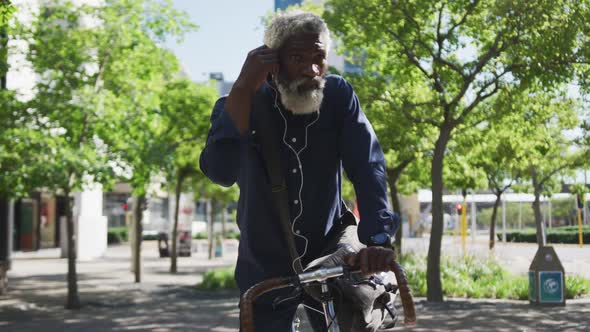 African american senior man sitting on bicycle wearing earphones on the road