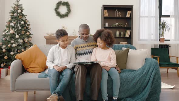 Senior African American Grandfather Reading Fairy Tale to Grandchildren Sitting Together at Home