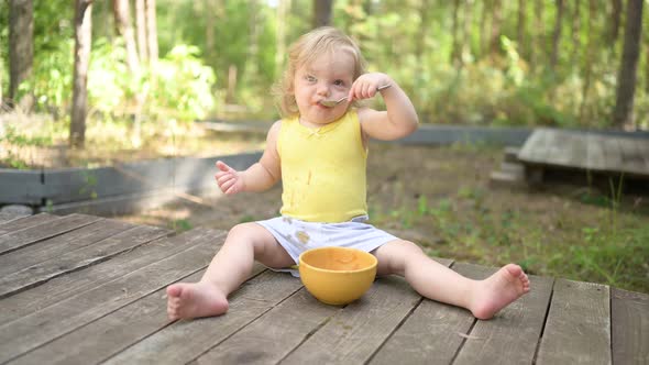 Little Funny Cute Blonde Girl Child Toddler with Dirty Clothes and Face Eating Baby Food Fruit or