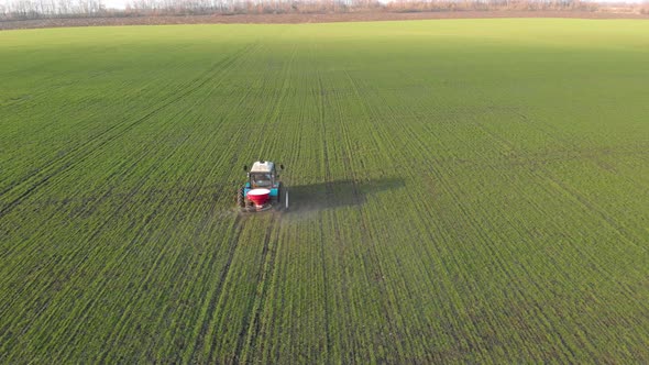 Tractor Spreading Artificial Fertilizers in Green Field. Farmer Fertilizing Arable Land with