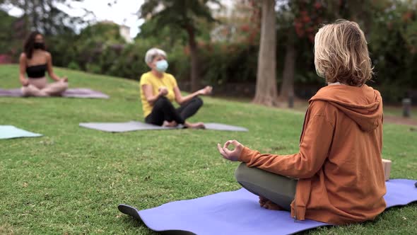 Multiracial people doing yoga class at park and sitting with social distance