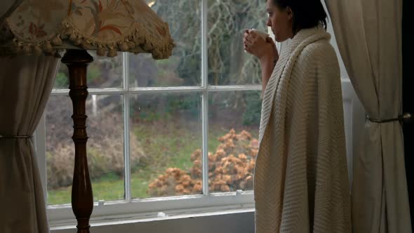 Beautiful woman standing near window and having cup of coffee