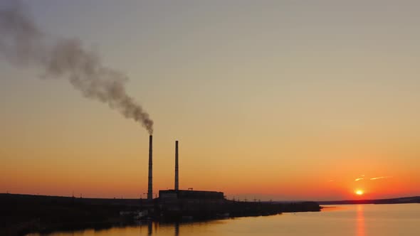 Plant with smoke against orange sky. Industry among nature at sunset. 