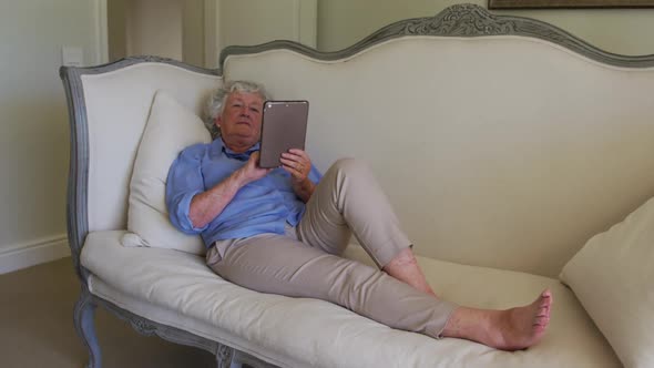 Caucasian senior woman using digital tablet while sitting on the couch at home
