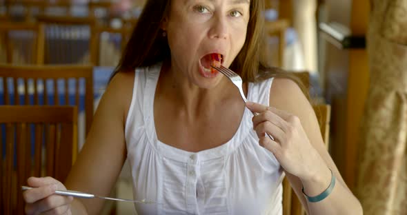 Adult Female Guest of Hotel Is Having Lunch in Restaurant, Eating Salad By Fork, Looking at Camera