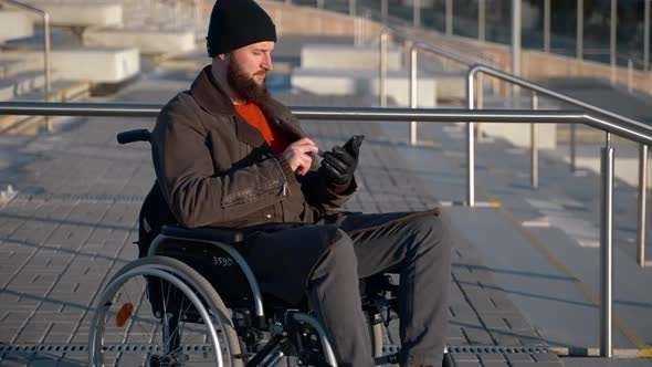 Wheelchairbound Man on Walk in City Using Social Networking in Smartphone