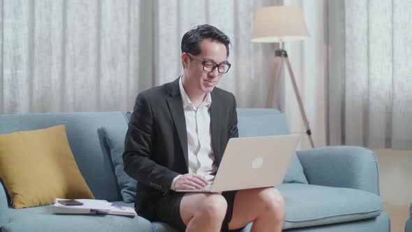 Asian Businessman In Jacket And Shorts Having Video Call On A Laptop At Home