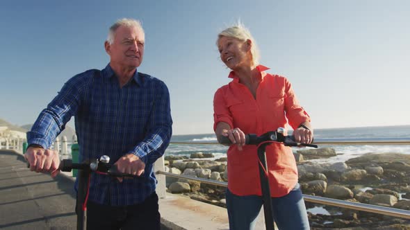 Senior couple walking next to electronic scooter alongside beach