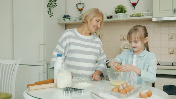 Little Girl Cooking Food with Granny's Guidance Breaking Eggs Mixing Ingredients in Kitchen at Home