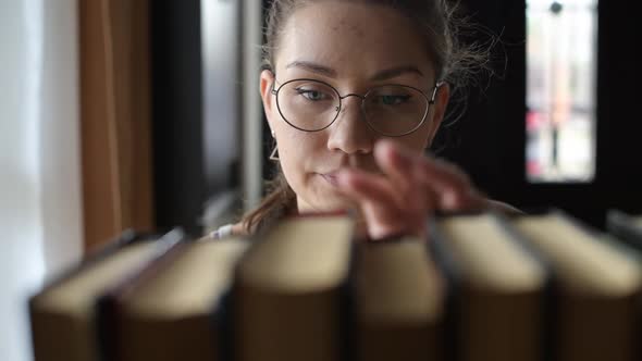 Girl student chooses a book and takes it from the shelf