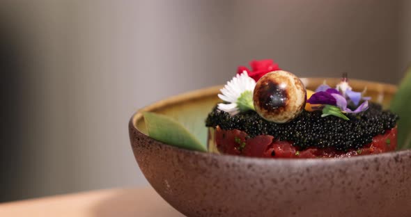 Salmon Sushi Roll Topped With Black Roe And Floral Garnishes - close up, tracking shot