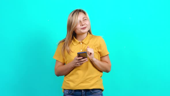 the Young Woman Uses the Phone on a Blue Background