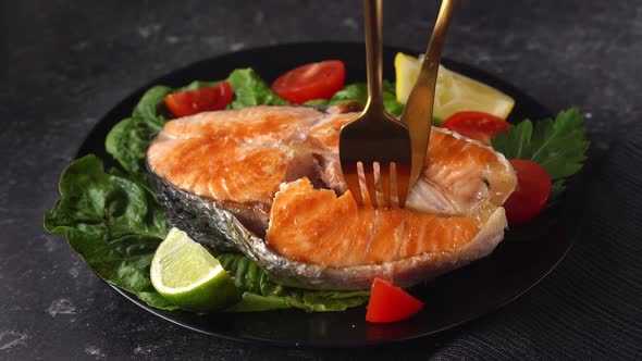 Close Up of a Grilled Salmon Steak in a Black Plate with Salad Leaves
