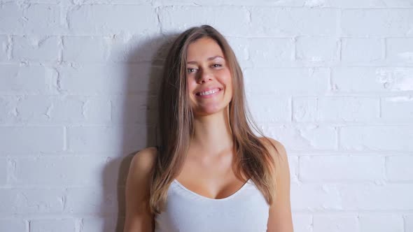 Young Attractive Female Smiling And Looking Seductive While Leaning Against A White Brick Wall 1