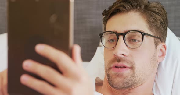 Smiling man wearing spectacles lying on bed using his tablet 4K 4k