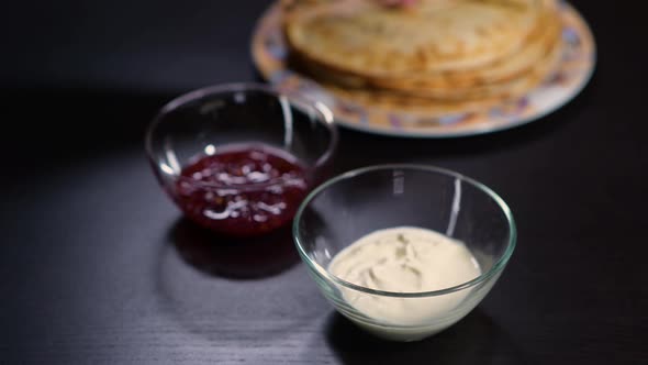 the girl s hand takes a twisted pancake and carefully dips it in sour cream