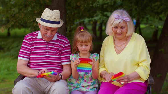 Smiling Senior Grandmother Grandfather with Granddaughter Playing Squeezing Antistress Toy Game